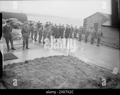 DIE ROYAL NAVY WÄHREND DES ZWEITEN WELTKRIEGS - HM König Georg VI. Auf dem Weg zur Inspektion der Marinekantine an der Küste von Scapa Flow. Auf beiden Seiten des Weges, auf dem er hinuntergeht, stehen Soldaten zur Aufmerksamkeit. Scapa Flow selbst ist im Hintergrund George VI., König zu sehen Stockfoto