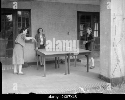 RASTSTÄTTE FÜR KRIEGSARBEITERINNEN: ERHOLUNG UND ENTSPANNUNG IN WALTON-ON-THE-HILL, SURREY, ENGLAND, Großbritannien, 1944 - zwei Kriegsarbeiterinnen genießen eine Partie Tischtennis auf der Veranda des Raststätte in Walton-on-the-Hill, während eine dritte Frau zusieht Stockfoto