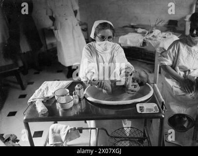 DAS HAUS WIRD ZUM ENTBINDUNGSHEIM: LIFE AT BROCKET HALL, WELWYN, HERTFORDSHIRE, 1942 - Eine Studentenschwester badet ein Baby in Brocket Hall. Die Krankenschwester trägt eine chirurgische Maske, um die Ausbreitung von Keimen zu verhindern Stockfoto