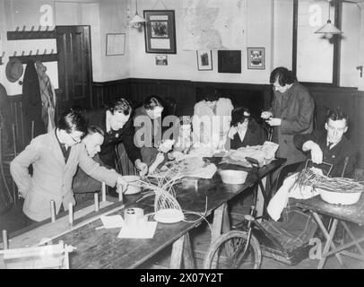 DIE ARBEIT DES CITIZENS' ADVICE BUREAU, ELDON HOUSE, CROYDON, ENGLAND, 1940 - Eine Gruppe behinderter Menschen stellt Körbe und andere Handarbeiten im Citizens' Advice Bureau in Croydon her. Diese Artikel werden später im Präsidium verkauft. Die Originalunterschrift für dieses Foto besagt, dass diese Kunsthandwerke sowohl das Hobby als auch die Lebensgrundlage dieser Menschen waren Stockfoto