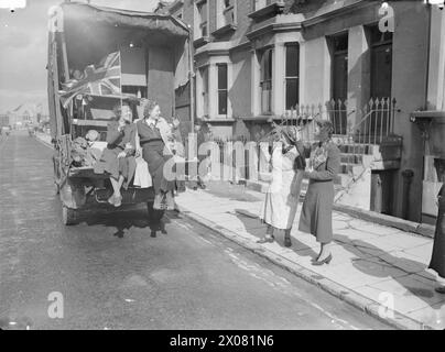 LONDON ZEIGT DIE FLAGGE: DAS LEBEN GEHT WEITER IN KRIEGSZEITEN LONDON, ENGLAND, 1940 - Mrs Cross, die Frau eines Seemanns, verabschiedet sich von ihren Nachbarn, als sie auf dem Rücksitz eines Umzugswagens von ihrem bombardierten Haus wegfährt. Ihr Freund, der ebenfalls im Truck sitzt, hält eine Gewerkschaftsfahne hoch Stockfoto