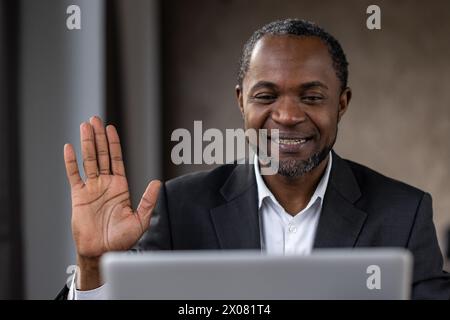 Ein Mann im Anzug lächelt und winkt der Kamera zu. Er trägt ein weißes Hemd und eine schwarze Jacke Stockfoto