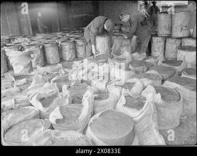 KÜCHENABFÄLLE IN VIEHFUTTER: BERGUNG AN DER BRITISCHEN HEIMATFRONT, 1942 - Arbeiter leeren Viehfutterkuchen aus den Mülltonnen, in denen sie in Säcken in einem Depot irgendwo in Großbritannien geformt wurden Stockfoto