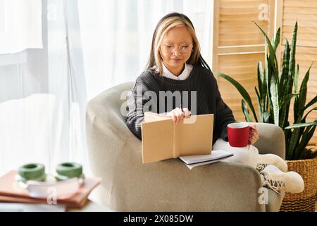 Eine junge asiatische Frau sitzt auf einem Stuhl, vertieft in ein Buch, während sie eine Tasse Kaffee genießt. Stockfoto