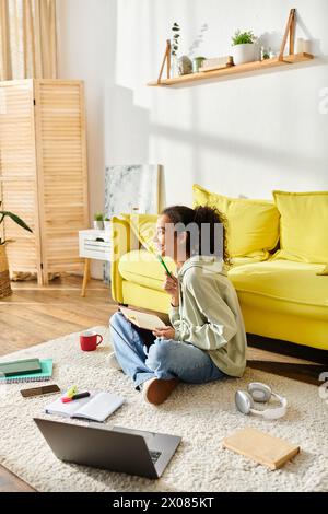 Ein Teenager sitzt auf dem Boden und beschäftigt sich mit E-Learning auf ihrem Laptop in gemütlicher Atmosphäre zu Hause. Stockfoto