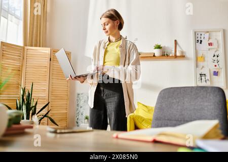 Ein zielgerichtetes Mädchen im Teenageralter, das in einem Raum steht und sich intensiv mit E-Learning-Aktivitäten auf ihrem Laptop beschäftigt. Stockfoto