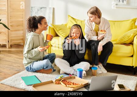 Drei junge Frauen verschiedener Rassen und Stile sitzen auf dem Boden und genießen gemeinsam Pizza in gemütlicher Atmosphäre. Stockfoto