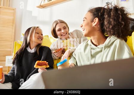 Eine vielfältige Gruppe Teenager-Mädchen lacht und plaudert, während sie auf einer Couch sitzen und zusammen leckere Pizza essen. Stockfoto