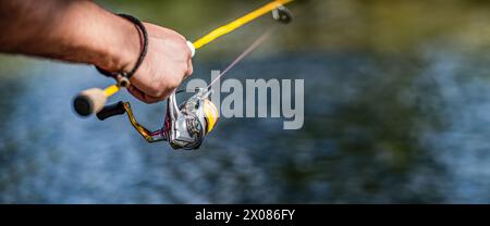 Fischer am Flussufer. Ein Fischer fängt einen Fisch. Fischer in der Hand, der sich dreht. Fisherman Hand hält Angelrute mit Rolle Stockfoto