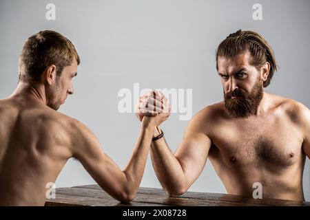 Arme ringen dünne Hand, großer starker Arm im Studio. Zwei Männerhände umklammten Arm Wrestling, stark und schwach, ungleiche Übereinstimmung. Stark muskulös bärtiger Mann Stockfoto
