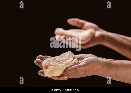 Alte Frauenhände, die einen braunen Brotlaib halten. Hilfe beim Brotteilen. Mann gibt Brot, hilft Hand Konzept. Eine helfende Hand mit einem Stück Brot Stockfoto