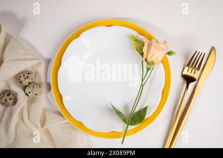 Wachteleier auf beiger Serviette, sanfte pfirsichfarbene Eustoma Blume auf weißen und gelben Tellern, goldenes Besteck auf zartem hellem pastellrosa Hintergrund. Ostern ta Stockfoto