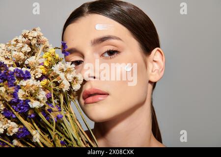 Eine junge Frau mit brünetten Haaren hält einen Blumenstrauß, während ihr Gesicht in einem Studio weiß gestrichen ist. Stockfoto