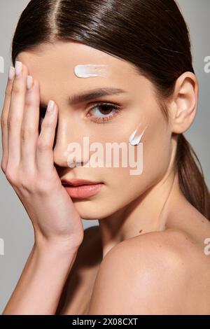 Eine junge Frau mit brünetten Haaren posiert in einem Studio-Setting und hält ihre Hand in einer kontemplativen Geste zart an ihr Gesicht. Stockfoto