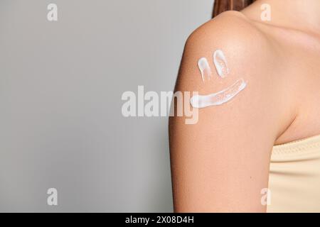 Eine junge Frau mit brünetten Haaren zeigt ein Lächeln auf ihrem Arm in einem Studio-Setting vor grauem Hintergrund. Stockfoto