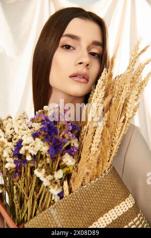 Eine junge Frau mit langen brünetten Haaren verströmt eine Sommerstimmung, während sie in einem Studio einen Strauß getrockneter Blumen hält. Stockfoto