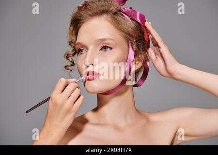 Eine junge Frau in einem Studio trägt Lippenstift auf ihre Lippen und konzentriert sich dabei auf die Verbesserung ihrer natürlichen Schönheit. Stockfoto