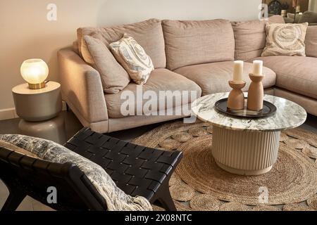 Ein geschmackvoll eingerichtetes, modernes Wohnzimmer mit gemütlichem beigefarbenem Sofa, stilvollem Marmor-Couchtisch und schicken Accessoires Stockfoto