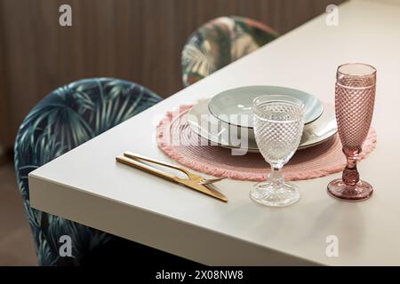 Ein schicker Esstisch mit stilvollem rosafarbenem Tischset, goldfarbenem Besteck und raffiniertem Glas auf einem modernen weißen Tisch Stockfoto