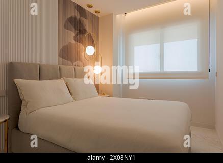 Modernes Schlafzimmer mit eleganter Beleuchtung, gemütlichem beigefarbenem Bett, künstlerischer Tapete und großem Fenster mit Tageslicht Stockfoto
