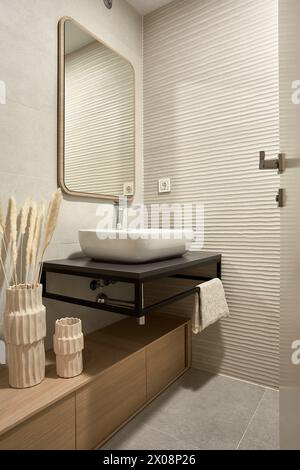 Modernes Badezimmer mit Waschbecken, strukturierten Fliesen, großem Spiegel und dekorativen Gegenständen Stockfoto