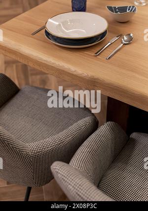 Ein stilvoller Tisch mit einem hölzernen Esstisch mit elegantem Geschirr und bequemen gemusterten Stühlen in einer warmen, einladenden Atmosphäre Stockfoto