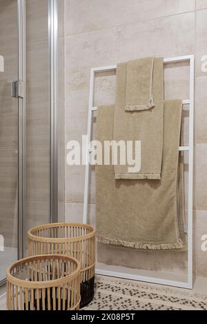 Ein modernes Badezimmer mit einem Handtuchleiter mit beigefarbenen Handtüchern und zwei stilvollen Holzkörben Stockfoto