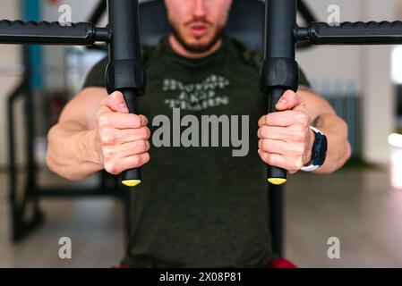 Nahaufnahme der Hände eines abgeschnittenen, nicht erkennbaren Mannes, während er im Fitnessstudio selbstbewusst einen Brustpresse verwendet und seine Fitnessroutine zeigt. Stockfoto