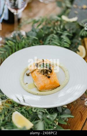 Perfekt gekochtes Lachsfilet mit zarten Pilzen, serviert auf einem weißen Teller mit Kräuterpüree, in festlicher Tischkulisse Stockfoto