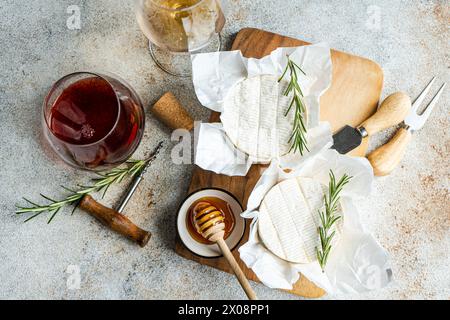 Blick von oben auf Rot- und Weißweingläser kombiniert mit Brie-Käse, Honig und Rosmarin auf einem Holzbrett, ideal für einen luxuriösen Snack oder eine Vorspeise. Stockfoto