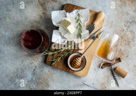 Ein Schuss Brie-Käse, frischer Rosmarin, Honig und ein Glas Rotwein auf einem rustikalen Holzbrett angeordnet. Stockfoto