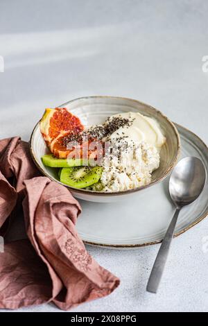 Eine nahrhafte Frühstücksschale mit cremigem Hüttenkäse, natürlichem Joghurt, Chiasamen, frischen Kiwis-Scheiben und einem saftigen Keil sizilianischer Orange Stockfoto