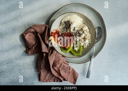 Von oben eine nahrhafte Frühstücksschale mit cremigem Hüttenkäse, natürlichem Joghurt, Chiasamen, frischen Kiwi-Scheiben und einem saftigen sizilianischen Keil Stockfoto