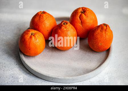 Eine Nahaufnahme reifer Clementinen, die ordentlich auf einer runden Betonplatte angeordnet sind, vor grauem Hintergrund Stockfoto