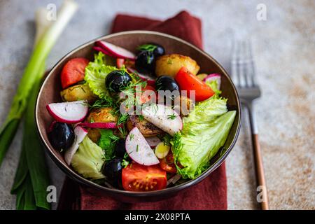 Nahaufnahme einer herzhaften Schüssel mit mediterranem Salat, garniert mit Dill, gebratenen Kartoffeln, Oliven, Kirschtomaten, Frühlingszwiebeln, knuspriges Lettu Stockfoto