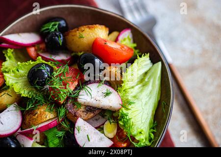 Eine Nahaufnahme einer köstlichen mediterranen Salatschüssel mit goldenen Kartoffeln, Reifen Kirschtomaten, schwarzen Oliven, Frühlingszwiebeln, Radieschen und Salat, ta Stockfoto