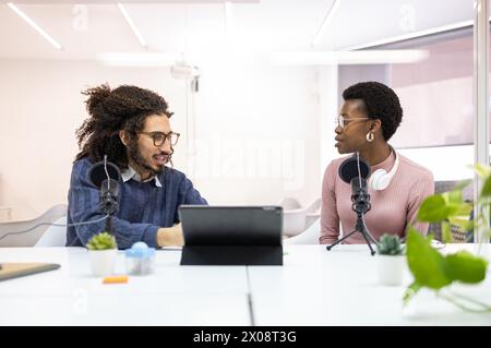 Ein hispanischer Mann und eine schwarze Frau nahmen an einer Diskussion in einem hellen Büro mit Podcast-Ausrüstung Teil. Stockfoto