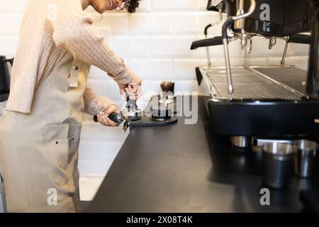 Eine hispanische Barista drückt gemahlenen Kaffee in einer professionellen Espressomaschine in einen Portafilter und bereitet sich auf die Zubereitung vor. Stockfoto