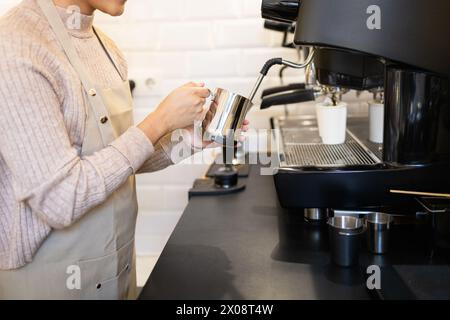 Ein fokussierter Barista nutzt eine moderne Espressomaschine, um Milch in einem Metallkrug zu dämpfen und sich auf ein cremiges Kaffeegetränk vorzubereiten. Stockfoto