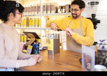 Fröhlicher hispanic man Barista, der einen Gast an einem modernen Café serviert. Stockfoto