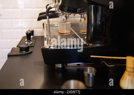 Nahaufnahme einer Espressomaschine, die frischen Kaffee zubereitet, wobei der reichhaltige Espresso in zwei klare Tassen auf einer Auffangschale fließt. Stockfoto