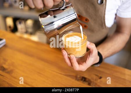 Ein erfahrener Barista gießt vorsichtig aufgeschäumte Milch in eine Tasse Espresso und kreiert so ein kompliziertes Latte Art Design. Stockfoto