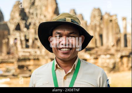 Ein fröhlicher männlicher Reiseleiter trägt einen Hut und lächelt warm vor dem berühmten Angkor Wat Hindu Tempel in Siem Reap, Kambodscha. Stockfoto