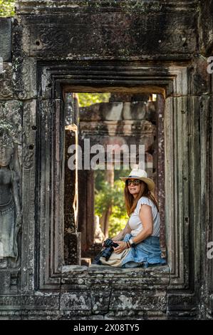 Eine weibliche Touristin mit weißem Hut wird unter den alten Steinrahmen des Tempelkomplexes Angkor Wat in Siem Reap, Kambodscha, mit Beruf fotografiert Stockfoto