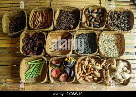 Verschiedene Gewürze in gewebten Körben, traditionell auf Bali, mit Zimt, Muskatnuss, schwarzem Pfeffer, Vanille und mehr auf einem rustikalen Holztisch. Stockfoto