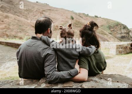 Ein herzerwärmender Moment einer Familie, die im Freien eng zusammensitzt und eine hügelige Landschaft überblickt, die ein Band der Liebe und Gesellschaft verbindet Stockfoto