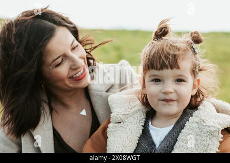 Eine glückliche Mutter und ihre kleine Tochter teilen einen liebevollen Moment auf dem Feld, mit aufrichtigem Lächeln und enger Umarmung Stockfoto