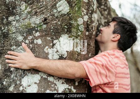 Eine Nahaufnahme eines Mannes in besinnlicher Umarmung mit einem großen, moosbedeckten Baum, der eine tiefe Verbindung zur Natur symbolisiert Stockfoto