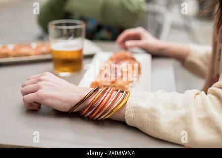 Bei einer Nahaufnahme wird der Arm einer Person mit bunten Armreifen aufgenommen, die auf eine entspannte Frühlingsatmosphäre hinweisen, während sie draußen mit Tapa und speisen Stockfoto