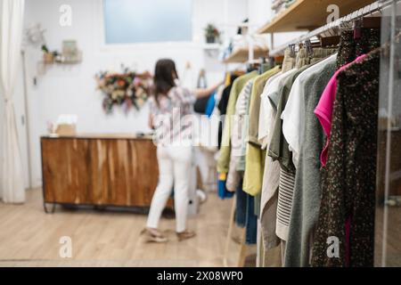 Zwei modische Frauen wählen Frühlingsoutfits aus einem Kleiderständer in einer Boutique mit gemütlicher Innenausstattung aus Stockfoto